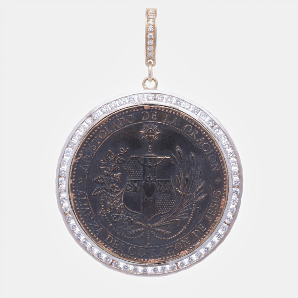 This Spanish Sacred Heart antiquity is original. The front translates to "Alliance of the Sacred Heart of Jesus". The back translates to "Live always interceding for us". The Latin words ADVE REGNVM- NIAT TVVM are to the left and right of Jesus. This original Spanish antiquity is set in a unique Cynthia Ann bezel. Constructed of 14k yellow gold 1.56g , channel set diamonds 1.23tcw, and sterling silver. The bale opens to 4mm. Spanish Sacred Heart Pendant