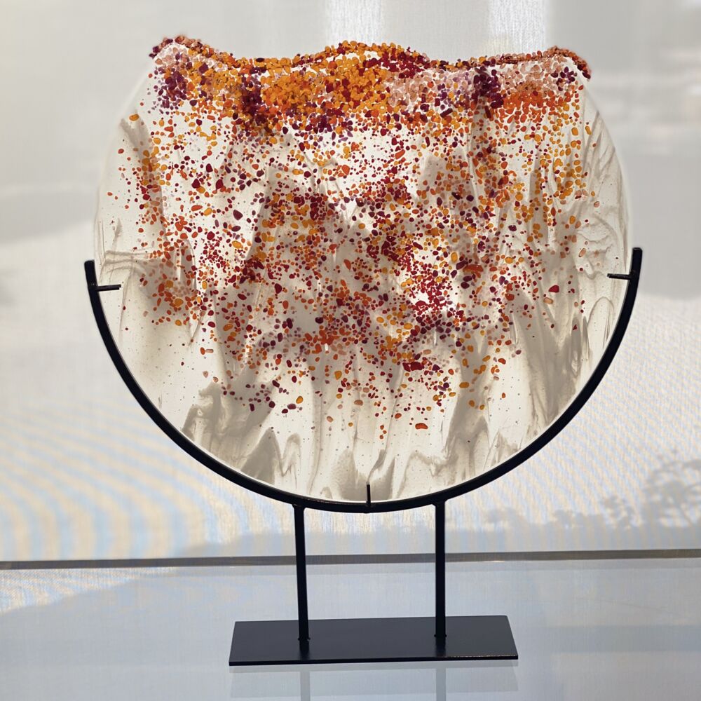 This semi-round sculpture by artist Carole Perry features crushed red and orange carnelian glass. Firewater Falls sits in a black steel frame. Fire Falls