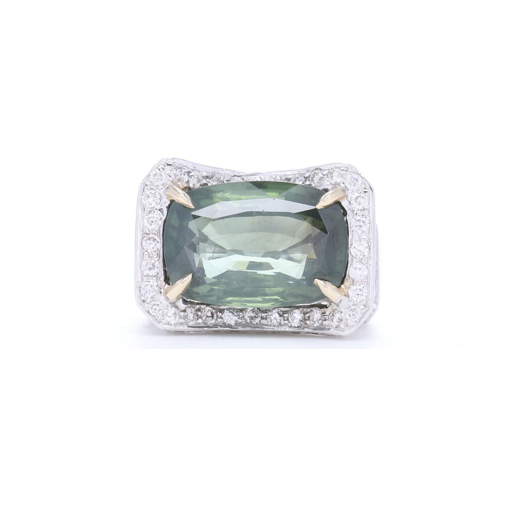 This one-of-a-kind stone is a tourmaline that changes hue a bit depending on light. Set in 18k white gold with diamonds around the mounting of the beautifully set elongated cushion cut green tourmaline, this is a cocktail ring you'll turn into your every day ring. Luxury feel in both look and weight of gold, this ring will be an heirloom passed down for generations. 18k White Gold Elongated Cushion Cut Green Tourmaline with Diamonds